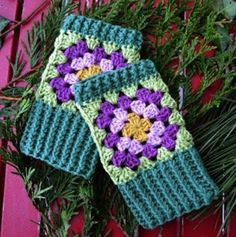 two green and purple crocheted mitts sitting on top of pine needles next to evergreen branches