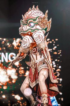 a woman in an elaborate costume walks down the catwalk at a fashion show with lights behind her