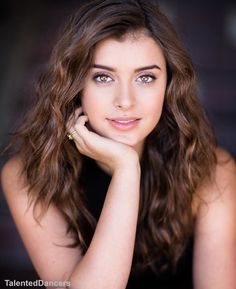 a beautiful young woman sitting at a table with her hand on her chin and looking into the camera