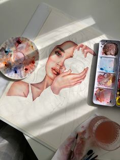 a woman's face is drawn on a piece of paper with watercolors and paintbrushes