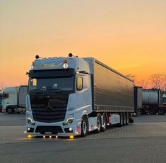 a semi truck is parked in a parking lot at sunset with other trucks behind it