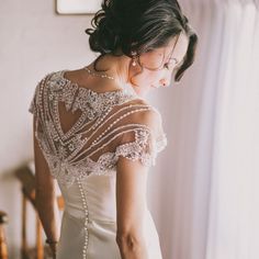 a woman standing in front of a window wearing a wedding dress with beading on it