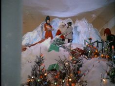 two people dressed as santa clause on top of a snow covered mountain with christmas trees