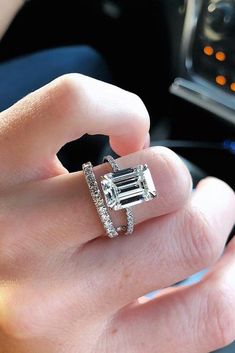 a woman's hand holding an engagement ring in the middle of her fingers,