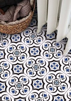 a black and white tile floor with blue designs in the center, next to a basket full of yarn