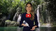 a woman standing in front of a waterfall holding a hair dryer and looking at the camera