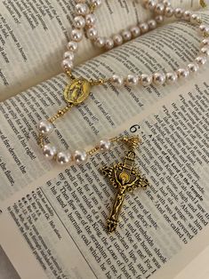 an open book with pearls and a cross on it's side next to a necklace