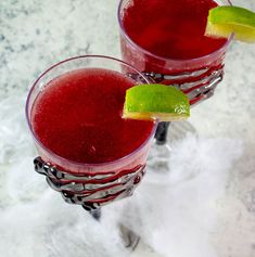 two glasses filled with red liquid and lime wedges