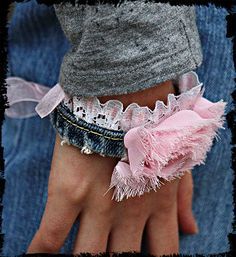 a person wearing a pink bracelet with lace on it's wrist and holding onto a pair of jeans