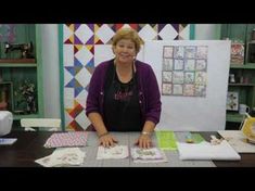 a woman sitting at a table with some quilts on it and papers in front of her