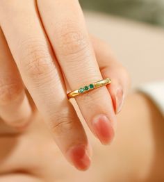 a woman's hand holding a gold ring with emeralds on it and the middle finger