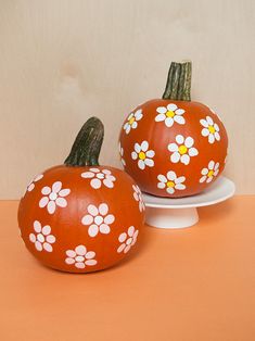 two painted pumpkins sitting on top of a white cake plate next to each other