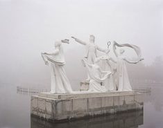 four statues are standing on the edge of a body of water