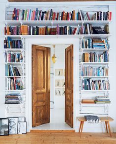 a bookshelf filled with lots of books next to two wooden doors in a room