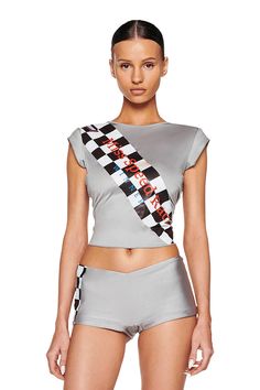 A woman is wearing the I.AM.GIA LARNIE TOP in grey, paired with high-waisted shorts. The crop top features a diagonal black and white checkered stripe with the text fast-paced fashion. She has her hair slicked back and stands against a white background. I Am Gia Corset, Iamgia Top, I Am Gia Shirts, I Am Gia Pink Set, I Am Gia Black Set, Sheer Bra, Tumblr Fashion, Festival Dress, Grey Women