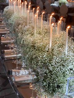 a long table with candles and flowers in vases on top of each other, along with place settings for the tables