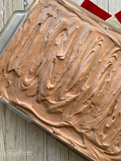 a cake with chocolate frosting in a pan on top of a wooden table next to a red ribbon