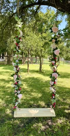 a wooden swing with flowers on it in the middle of a grassy area under a tree