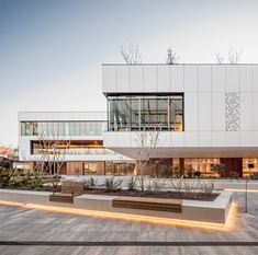 the building has many windows and lights on it's front side, along with benches