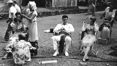 an old black and white photo of people sitting on lawn chairs in the grass with instruments