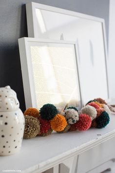 a white vase sitting on top of a table next to a framed photo and pom - poms