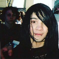 a girl with black hair and piercings on her nose looking at the camera while standing in front of other people