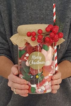 a person holding a jar filled with candy canes and christmas candies in it