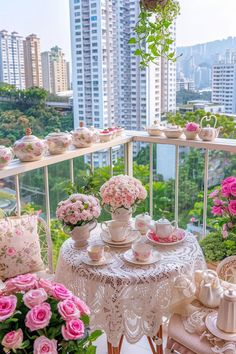 a balcony with pink flowers and tea set on it, overlooking the cityscape