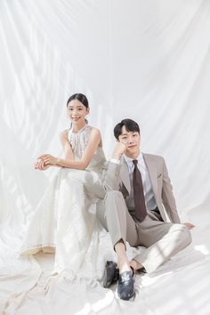 a man and woman sitting on the ground in front of a white backdrop wearing formal clothes