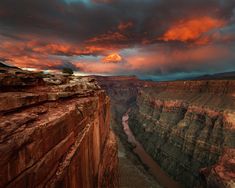 the sun is setting at the edge of a cliff with a river running through it