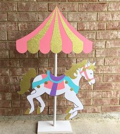 a paper cutout of a carousel horse on a white stand with pink and gold glitters