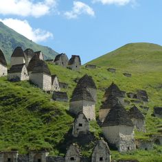 an old village on the side of a hill with grass growing all around it and mountains in the background