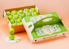 an open box of green apples sitting on top of a pink surface next to another box