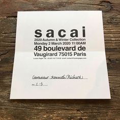 a piece of paper that is on top of a wooden table and has the words sacai written in black