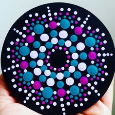 a hand holding up a black and purple polka dot design paper coaster with white dots on it