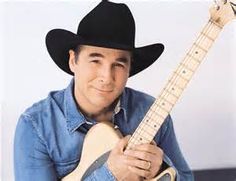 a man wearing a cowboy hat holding a guitar in his right hand and looking at the camera