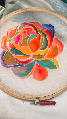 a colorful flower is painted on a white cloth with a wooden frame and some paintbrushes