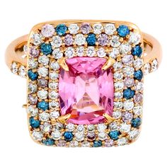 This enchanting ring boasts a central 1.51-carat cushion-cut pink sapphire, radiating elegance and charm. Surrounding the sapphire are three exquisite halos: the first halo features white round diamonds; second and third halos enhance the design with a harmonious blend of white, pink, and blue round diamonds—66 white diamonds (0.68 carats) 15 pink diamonds (0.18 carats) and 15 blue diamonds (0.16 carats). Adding a unique flair, 10 side-drilled diamonds weighing 0.97 carats elegantly dangle around the setting, creating a captivating movement. Crafted in 14k pink gold weighing 5.03 grams, this ring is a standout piece, perfect for any party or special occasion. Its eye-catching design, especially the dangling diamonds, ensures it will capture attention and admiration. Perfect for day and nig Colored Diamond Rings, Gold Cocktail, Gold Cocktail Ring, Modern Ring, Sapphire Stone, Color Ring, Yellow Sapphire, Sapphire Gemstone, Pink Diamond