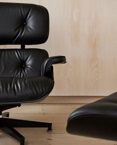 an eames chair and ottoman in front of a wooden wall