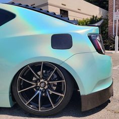 the rear end of a blue car parked in front of a building with green hologish paint on it