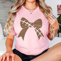 Score a touchdown with our Football Large Bow Bella Tee! Gear up for game day in style with our Football Large Bow Bella Tee, the perfect blend of sporty chic and feminine flair. Crafted from premium, ultra-soft fabric, this tee is as comfortable as it is stylish, making it the ideal choice for cheering on your favorite team from the stands or enjoying a casual day out with friends. The standout feature? A large bow, right on trend with football stitching, adding a touch of playful charm to the classic football-inspired design. But it's not just about looks – our Bella Tee is designed with your comfort in mind, so you can focus on the game without any distractions. The relaxed fit and breathable fabric keep you cool and comfortable, inning after inning. Available in a range of colors, our Pink Game Day Top With Team Spirit, Pink Team Spirit Tops For Game Day, Team Spirit Pink Tops For Game Day, Pink Team Spirit Game Day Top, Pink Tops For Game Day With Team Spirit Style, Casual Tops For Cheerleading In Fall, Pink Sporty T-shirt For Fall, Cheerleading Tops For Fall, Sporty Pink Tops For Game Day