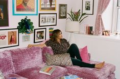 a woman sitting on top of a pink couch in a living room next to a window