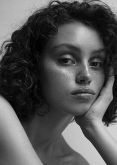 black and white photograph of a woman with curly hair looking at the camera while holding her hand to her face