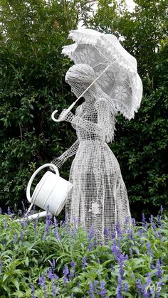 a woman with an umbrella and watering can is in the middle of some purple flowers