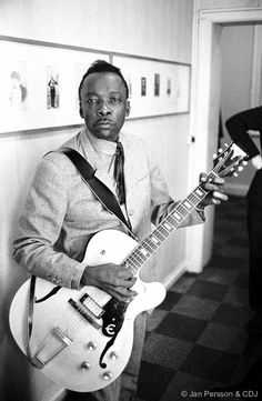 a black and white photo of a man playing an electric guitar in a hallway with another man standing next to him