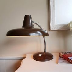 a desk lamp sitting on top of a white table next to a book and vase