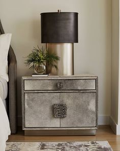 a nightstand with a lamp on top of it next to a bed