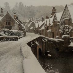 a snowy street lined with houses next to a small river in the middle of town