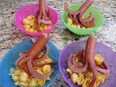 four plates with different types of food in them on a counter top, including hot dogs and macaroni and cheese