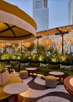 an outdoor seating area with tables and umbrellas on the roof terrace in front of high rise buildings